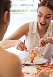 A woman at a restaurant smiles while serving herself a slice of pizza with a man across the table from her.